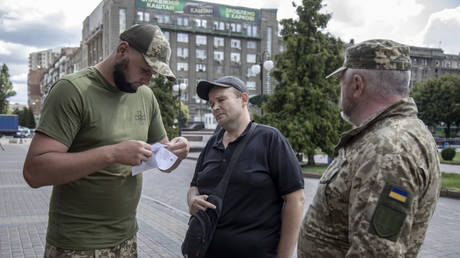 Ukrainian recruitment officers check a civilian’s documents during street patrols targeting men of fighting age.